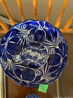 Top view of large blue ceramic decorative bowl with white floral patterns inside, shows scalloped rim.