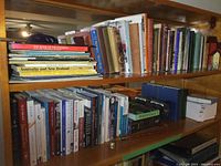 Wide shot of two wooden shelves filled with books, a flag, a candle snuffer, a bookend and a box of thank you cards.