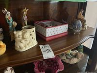 Shelf of various bunny and chick figurines including snowman salt and pepper shakers, a box set of mug and coaster, and a music box shaped egg.