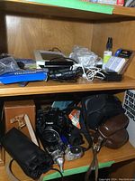 Shelf view showing Canon PowerShot SX50HS with strap, battery charger, assorted cables, digital picture frame and other electronics