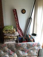 Image of stacked floral cushions alongside colorful lounge cushions and outdoor mat rolled vertically. Various items including umbrella bag visible.