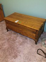 Wooden chest from an angled front-left perspective showing the hinged top and carved legs.
