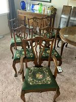 Overview of all six chairs showing wooden frames, carved backs, and green needlepoint seats with floral design.