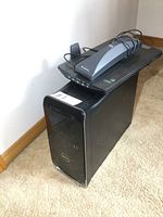 Dell XPS desktop tower with HP Scanjet scanner placed on top against a wall on carpeted floor.