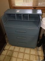 Front view of blue painted dresser showing three drawers and desk area with four cubby compartments.