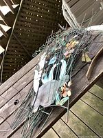 Decorative metal garden trellis with bird, flowers, and butterfly motifs, showing rust and weathering, lying on wooden table.