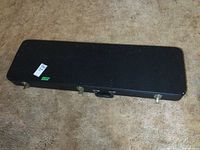 Closed guitar case showing black textured exterior, metal latches, and handle.