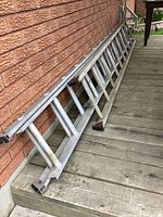 Aluminum extension ladder leaning against brick wall on wooden deck showing length, material, and wear.