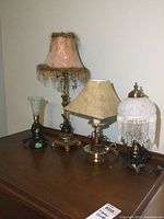 Four different decorative table lamps on wooden surface against beige wall.