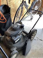 Side view of the lawn mower showing engine, wheels, handle, and mulch bag.