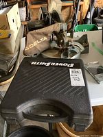 Photo of Delta mitre saw on table with dust bag attached and black hard case labeled Power Smith in front.