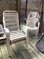 Stacked white plastic lawn chairs showing weathering and dirt marks on porch wooden deck