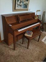 Full view of upright piano with bench, brass piano lamp on top, and vintage music books resting on the bench.