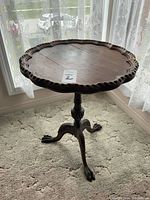 Full view of the round wooden table with scalloped edge placed in front of a window.