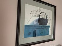 Angled view showing the framed signed print with a focus on the basket and cabinet image.