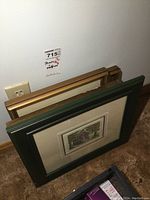 Side view of four framed artworks stacked upright against a wall showing varying frame colors and sizes.