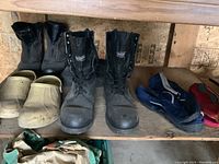 Men's black boots and multiple water shoes placed on wooden shelf, showing condition and variety.