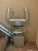 Beige seat assembly with foldable armrests and footrest mounted at base of rail