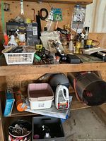 Wide view of shelf with assorted tools, hardware, sprays, plastic containers, funnel, and Black & Decker drill