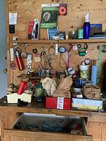 Workbench area with assorted hand tools, packs of nails, screws, tapes, varnishes, small hardware containers and utility items hanging and placed on the workbench.