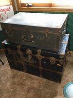 Two vintage trunks stacked, smaller green trunk labeled MALE on top of larger black trunk.