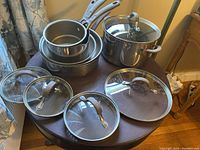 Eleven-piece Circulon stainless steel cookware set arranged on a table, showing frying pans, saucepots, stock pot, sauté pan, and various glass lids.
