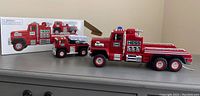 Side view of two Hess firetruck toys with box in background.