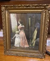 Front view of the antique picture and ornate gilded frame showing mother and daughter looking out window with harp in background.