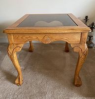 Front angled view of wooden end table showing carved legs and glass top.