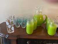 Photo showing the full set of glassware including the green pitcher, matching green glasses, and two styles of highball glasses with decorative patterns.