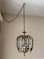 Gold metal hanging chandelier with crystal prisms and four candle-style lights hanging from ceiling by long metal chain.
