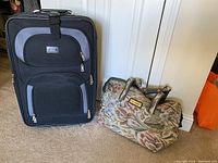 Full view of large black rolling luggage and floral Gloria Vanderbilt overnight bag on the floor