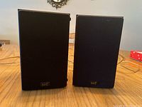 Pair of vintage NHT speakers shown front-facing with black fabric grille and logos visible, placed on wooden surface.