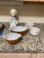 Image of the lot showing Mother Goose cookie jar, two Halls ceramic bowls with floral print, and two Pyrex mixing bowls with brown-orange fruit pattern