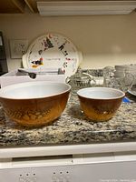 Two Pyrex brown Gooseberry Dot pattern mixing bowls front and center on granite countertop with other items behind