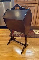 Side-angle photo of the vintage wooden sewing box on its stand showing the slanted top and base support legs.