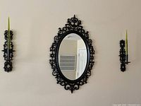 Full view of oval mirror with ornate black resin frame and two matching candle holders on each side with green glass candles.