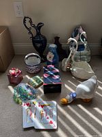 Photo showing collection of vintage decorative items: large blue vase, two white ceramic swan and duck planters, small gift boxes, a bag of marbles, small ceramic bowl and card shuffler boxed.