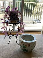 Wandering Jew plant in blue and white ceramic pot on black metal plant stand, next to decorative ceramic planter with floral and butterfly designs