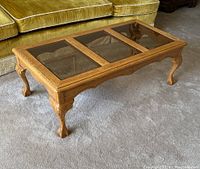 Wooden coffee table from an angle showing all three beveled glass panels and carved legs.