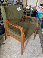 Angle view of the mid-century modern accent chair showing wooden frame with angular armrests and olive green cushioned seat and back.