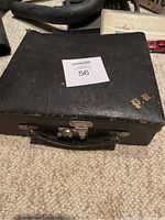 Front angle view of black leather vintage embroidery kit box with maxsold lot label on top