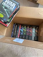 Box containing Babylon 5 complete series and other DVDs, showing stacked DVD cases in cardboard box