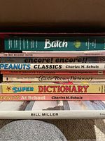 Spine view showing the titles of assorted comic and Peanuts books including Peanuts Classics, Charlie Brown Dictionary, Super Dictionary, and more.