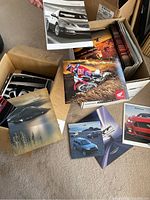 Box showing a variety of car brochures including Ford Mustang and Honda dirt bike covers.