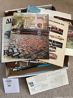 Box filled with assorted vintage car brochures including prominently a 1981 Chrysler Cordoba brochure with car on cobblestone street.