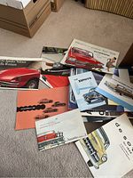 Overview photo showing multiple vintage car brochures spread on carpet including Porsche, Alfa Romeo, Plymouth, Buick, and others.