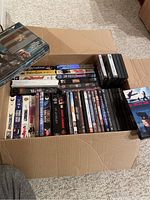Wide shot of the box showing stacked DVDs and VHS tapes with visible titles and covers.
