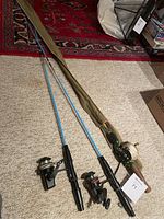Three vintage fishing rods laid out on carpet; one rod with a green baitcasting reel and olive canvas sleeve, two rods with spinning reels; the rods are blue with black handles.