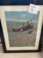 Photo of framed World War 1 airplane print, showing two aircraft flying above terrain.